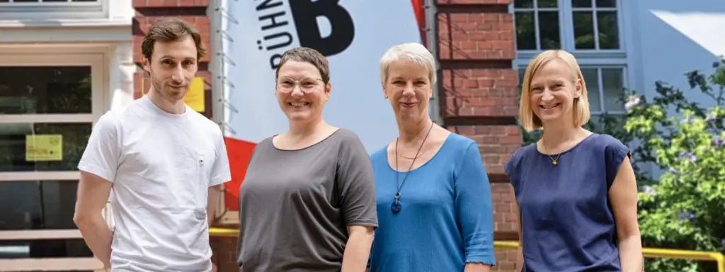 Des Team vom B-Treff bestehend aus drei Frauen und einem Mann, die vor dem Eingang des B-Treff stehen und lächeln