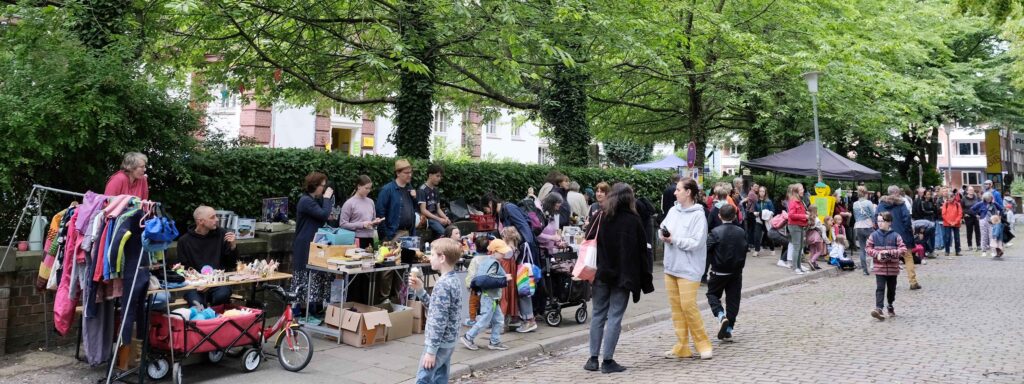 Flohmarktstände vor dem B-Treff unter grünen Bäumen bei Sommerwetter