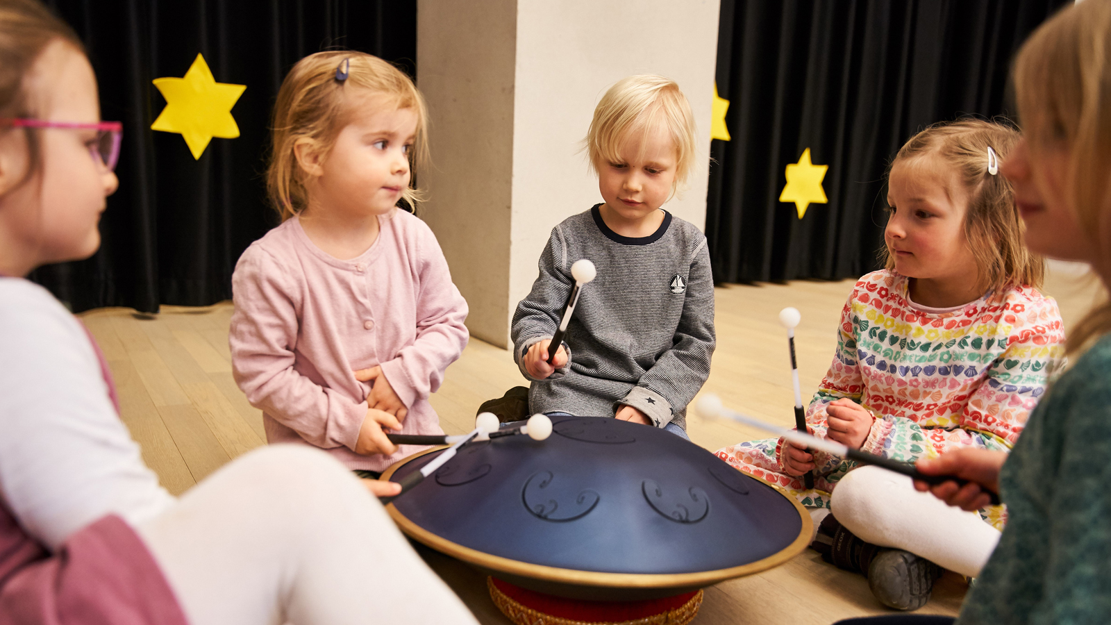 Kinder sitzen um eine Handpan und spielen sie