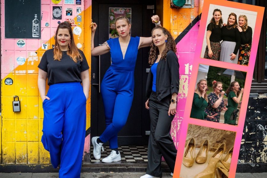 Die drei Chorsängerinnen posieren in knallblauen und schwarzen Outfits vor einer bunten Wand
